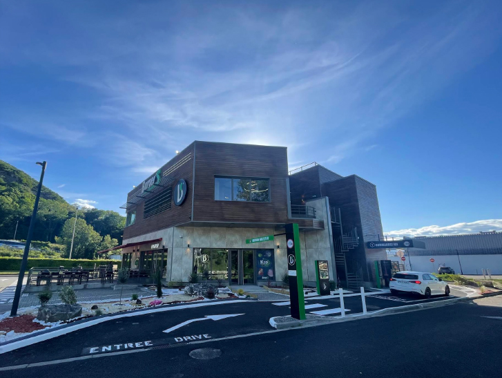 Modern two-stages commercial building with outdoor seating and drive-through signage under a blue sky
