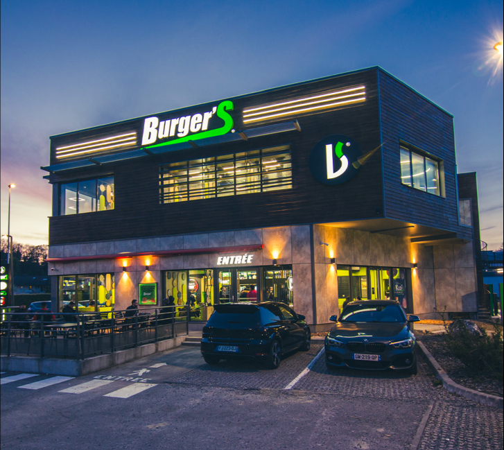Exterior of a Burger'S restaurant at dusk with cars parked outside and illuminated signage