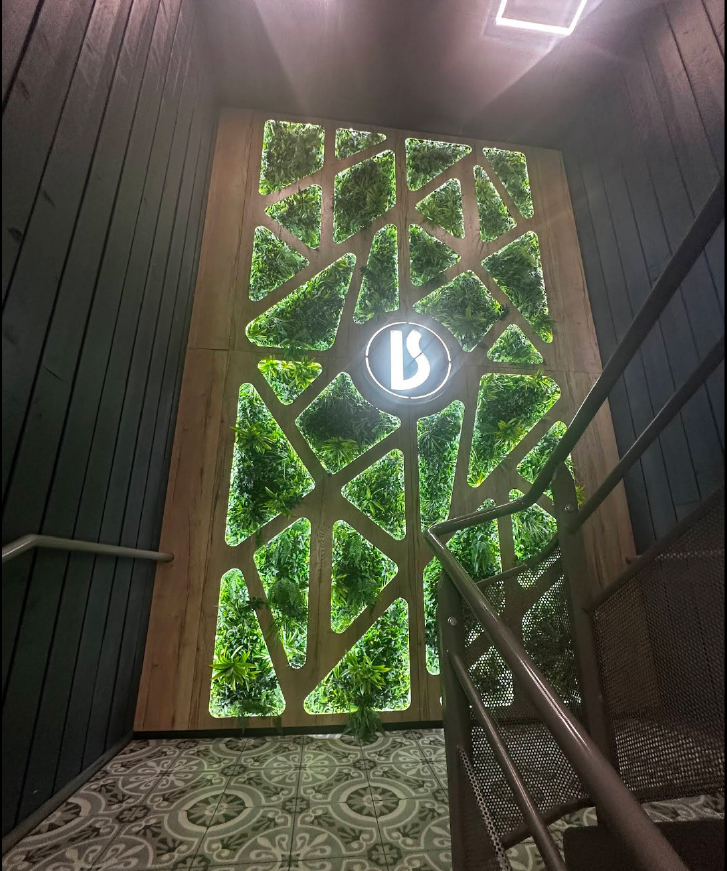 Stairwell with decorative wall panel featuring geometric cutouts filled with plants and a circular illuminated logo in the center